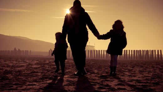 Ouder met twee kleine kinderen op het strand met avondzon. 